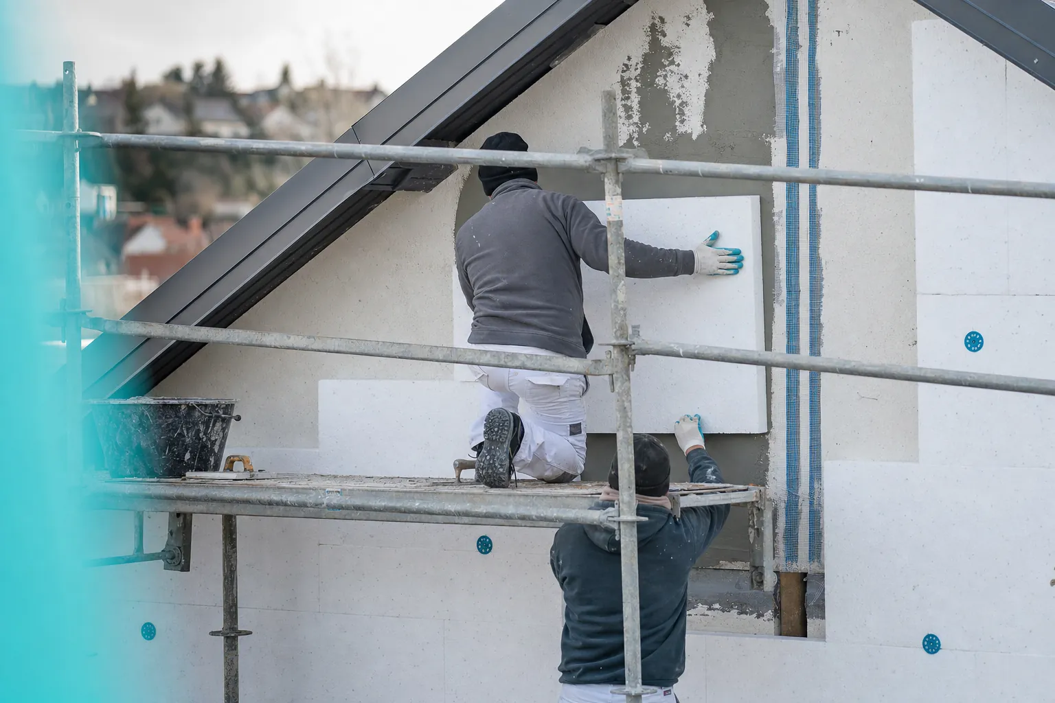plan large d'un pignon de maison couvert de panneaux isolants blancs en cours de pose, echafaudage devant, sous-enduit arme